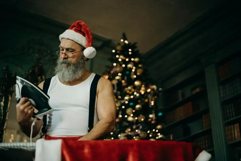 Papá Noel planchando con luces navideñas de fondo, un ejemplo de ahorro de energía en Navidad